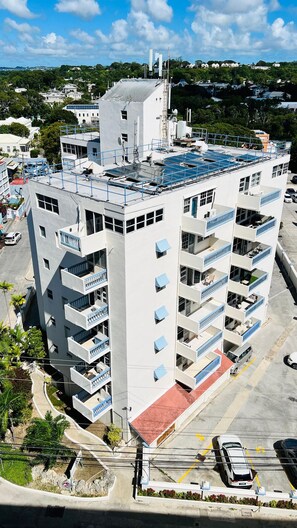 A multi-story building with balconies, a parking area, and a clear sky.