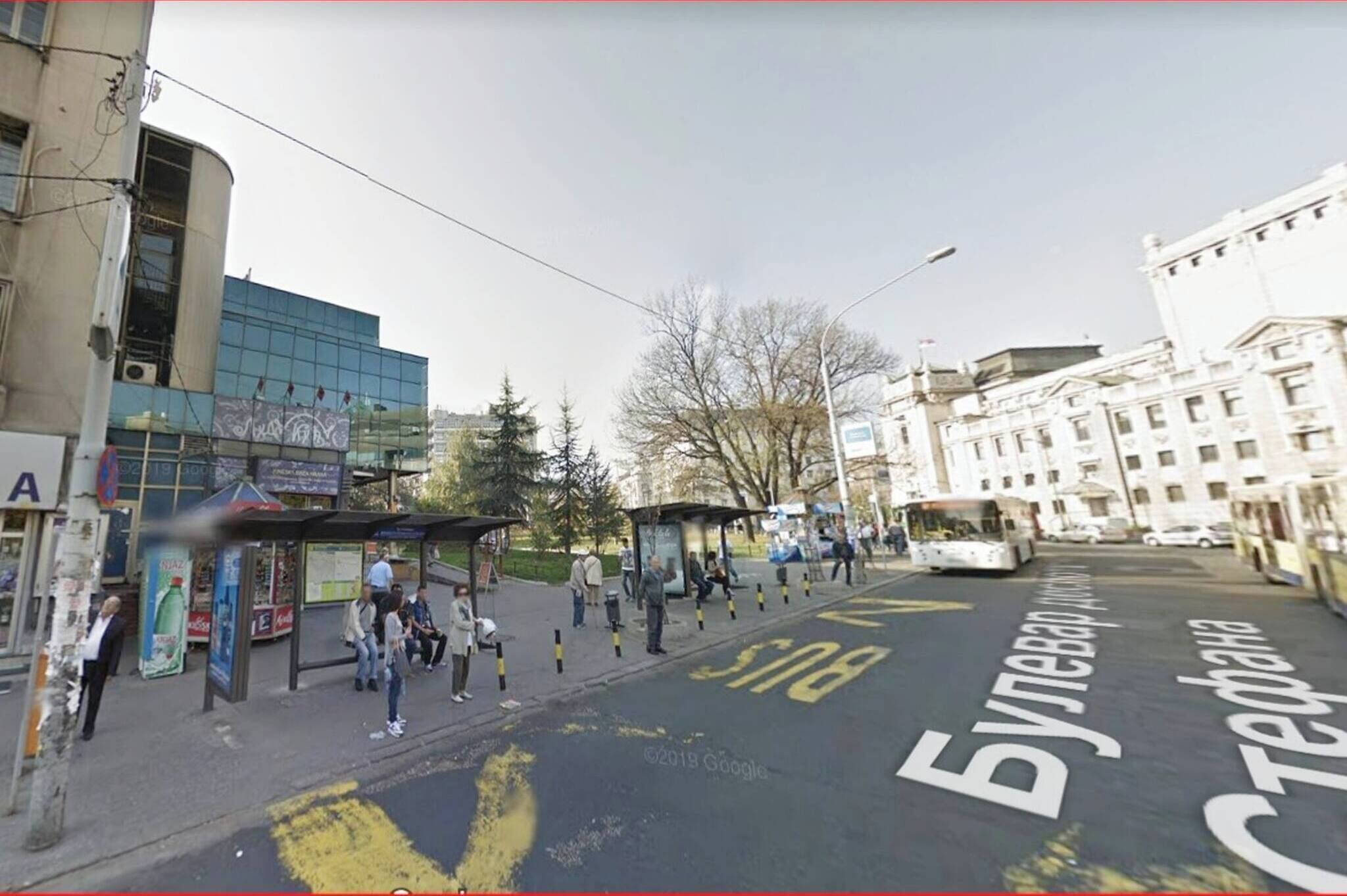 A bus stop with a shelter, a bus, and a building with a large glass facade.