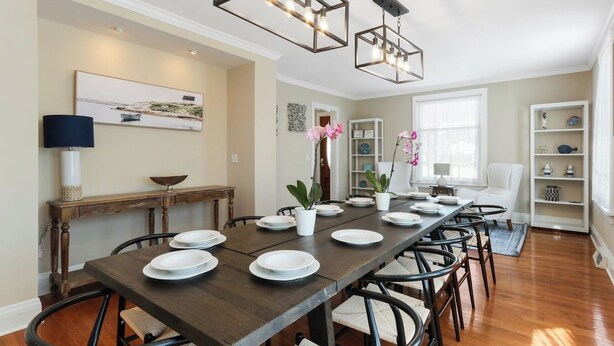 Comedor con una larga mesa de madera dispuesta para seis personas, rodeado de sillas con asientos de mimbre.