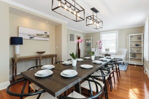 A dining area with a long wooden table set for six, surrounded by chairs with woven seats.