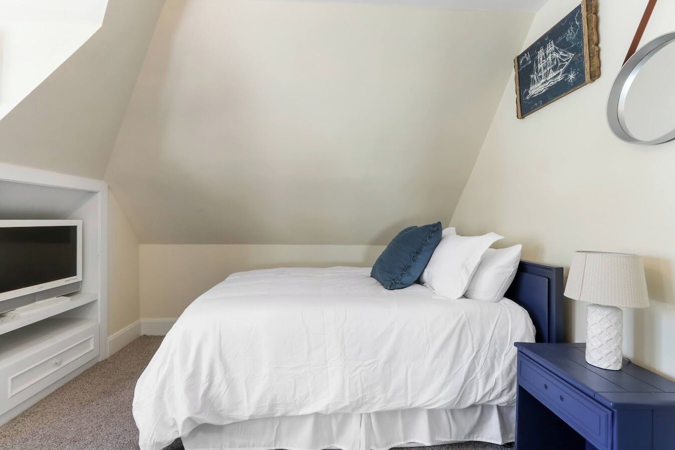 Ein Schlafzimmer mit Bett, Fernseher, Lampe und einer Wandillustration eines Schiffes.