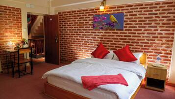 Habitación de hotel con pared de ladrillo, cama con almohadas rojas, mesita de noche de madera y un cuadro de un pájaro.