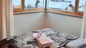 A bedroom with a large bed, two windows, and a view of a snowy landscape. - Adventure Panorama (Warth)