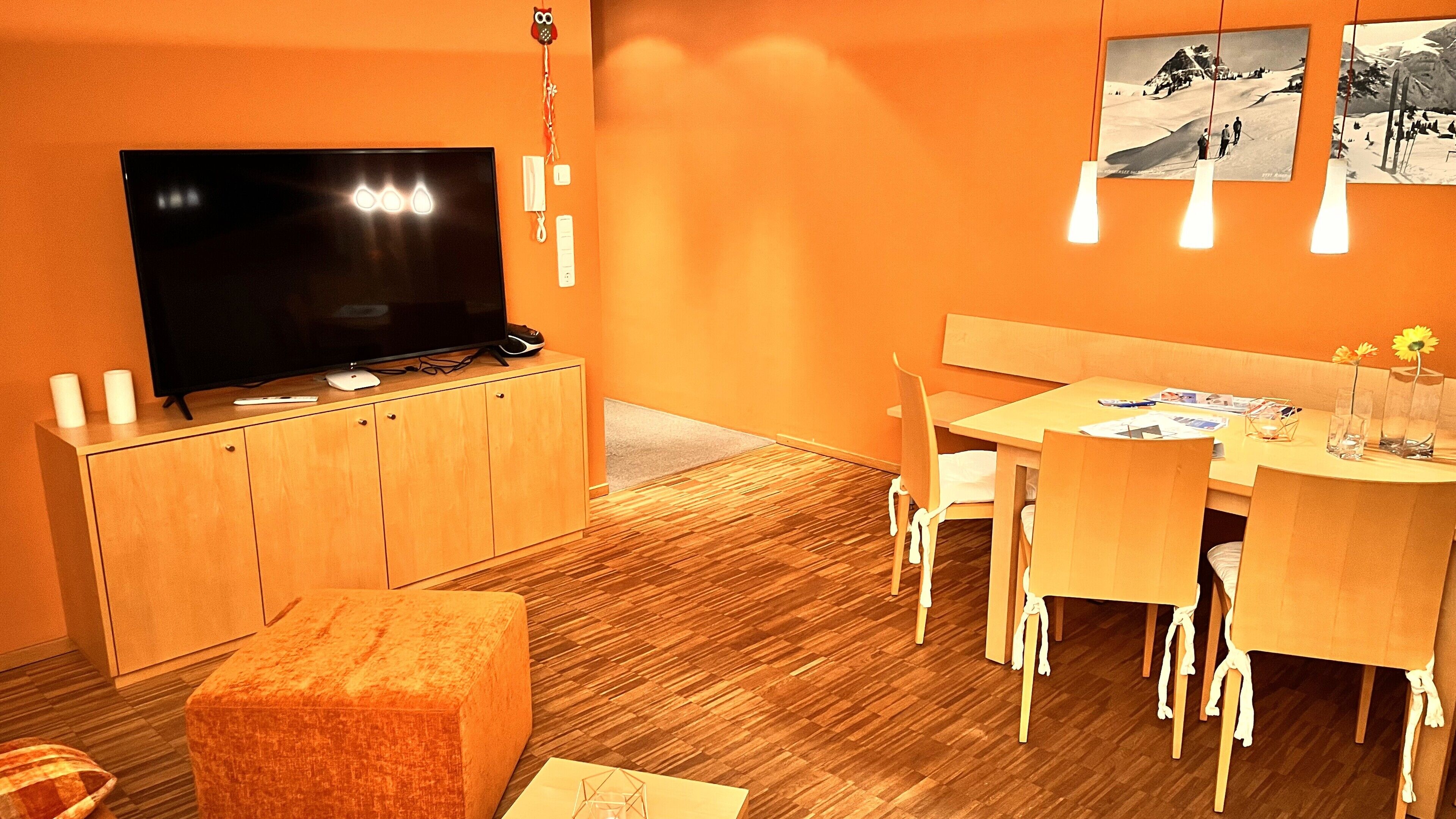 Ein modernes Wohnzimmer mit Flachbildfernseher, Holzmöbeln und einem Essbereich mit Tisch und Stühlen.