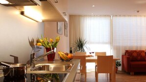 A modern kitchen with a stainless steel sink, a dining area with a table and chairs, and a red sofa in the living room. - Adventure Panorama (Warth)
