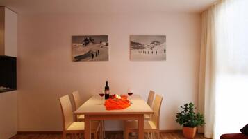 A dining area with a table, chairs, a bottle of wine, and two framed pictures on the wall.