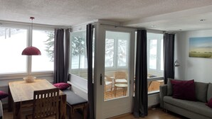 A cozy room with a wooden dining table, a sofa, and a view through a glass door to an outdoor deck. - Adventure Panorama (Warth)