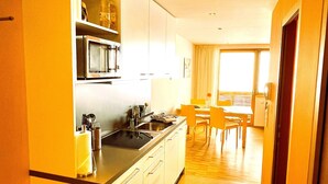 A compact kitchen with a microwave, sink, and cabinets, leading to a dining area with a table and chairs. - Adventure Panorama (Warth)
