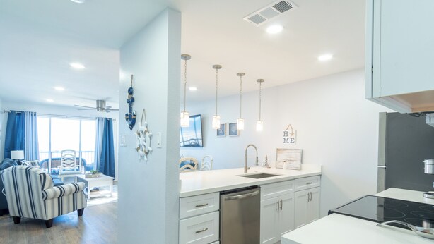 A modern kitchen with white cabinetry, a dishwasher, and a black stove. There is a dining area with a striped chair and a table.