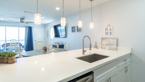 A modern kitchen with a white countertop, stainless steel sink, and pendant lights.