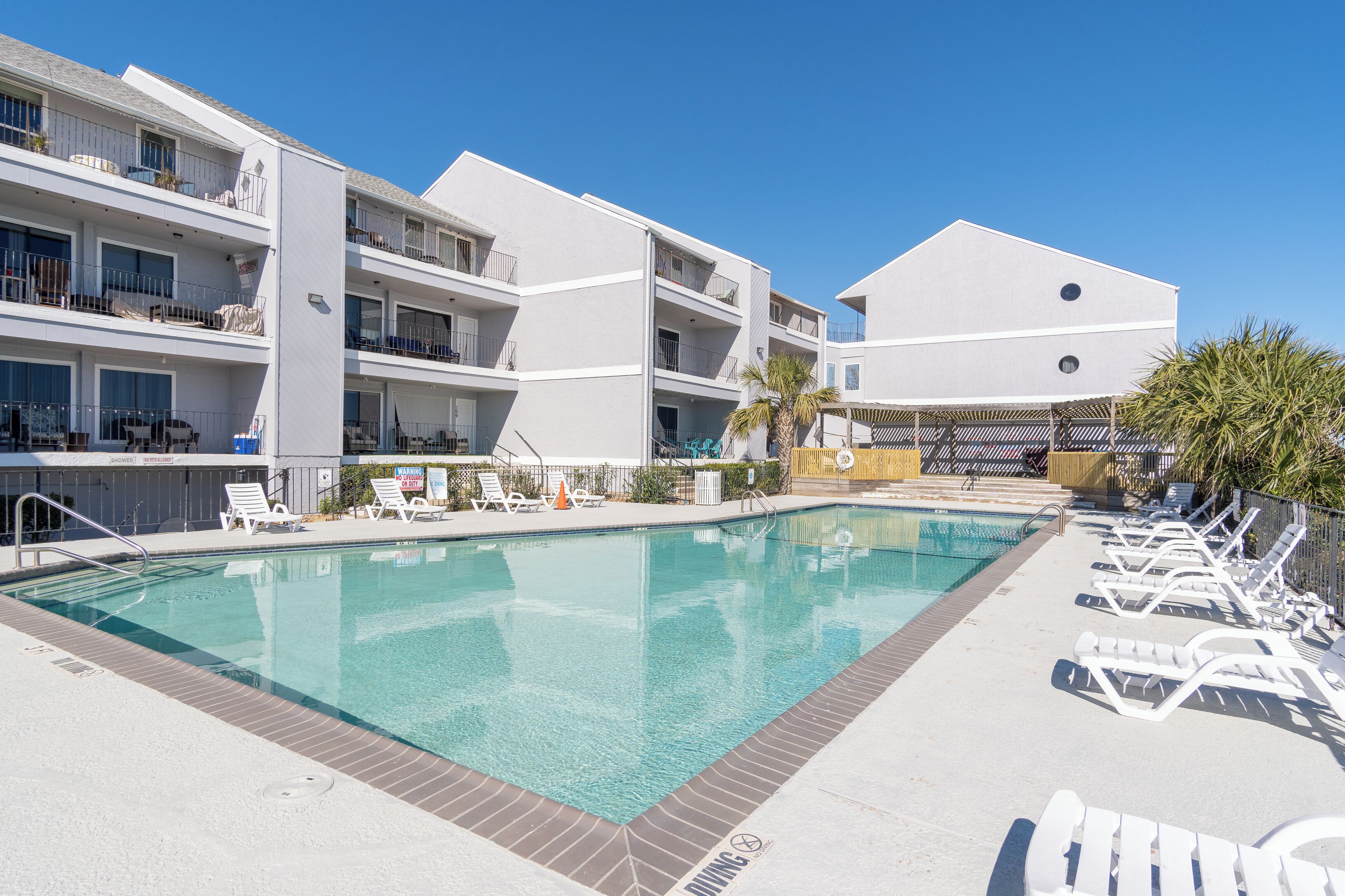 A swimming pool with lounge chairs and a building with balconies.