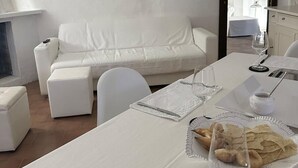 Zona pranzo con tavolo bianco apparecchiato per due, con piatti, posate e bicchieri.