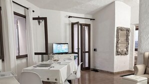 Un'area ristorazione moderna e ben illuminata, con un tavolo bianco apparecchiato per due, una televisione e un grande specchio.