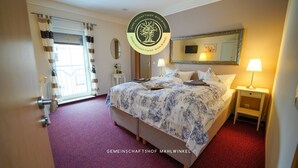 A hotel room with a bed, bedside tables, a mirror, a window with curtains, and a red carpet.
