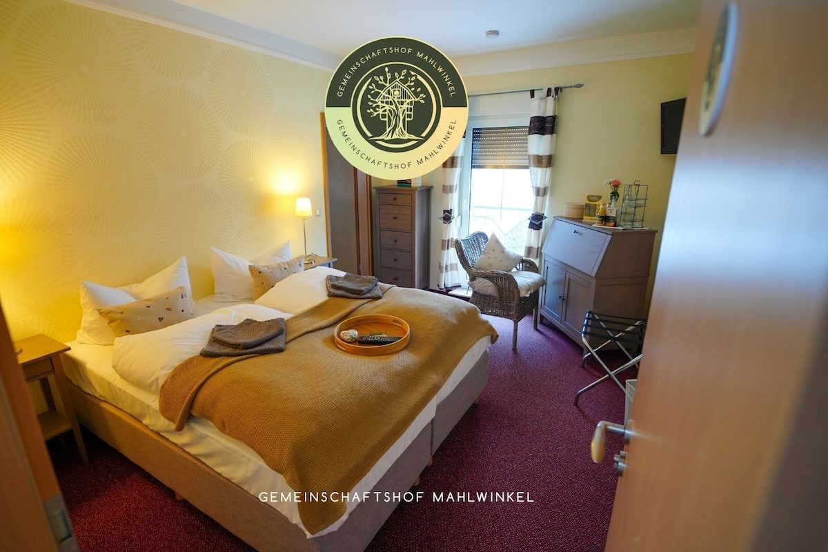 A hotel room with a bed, a chair, a desk, and a window with curtains.
