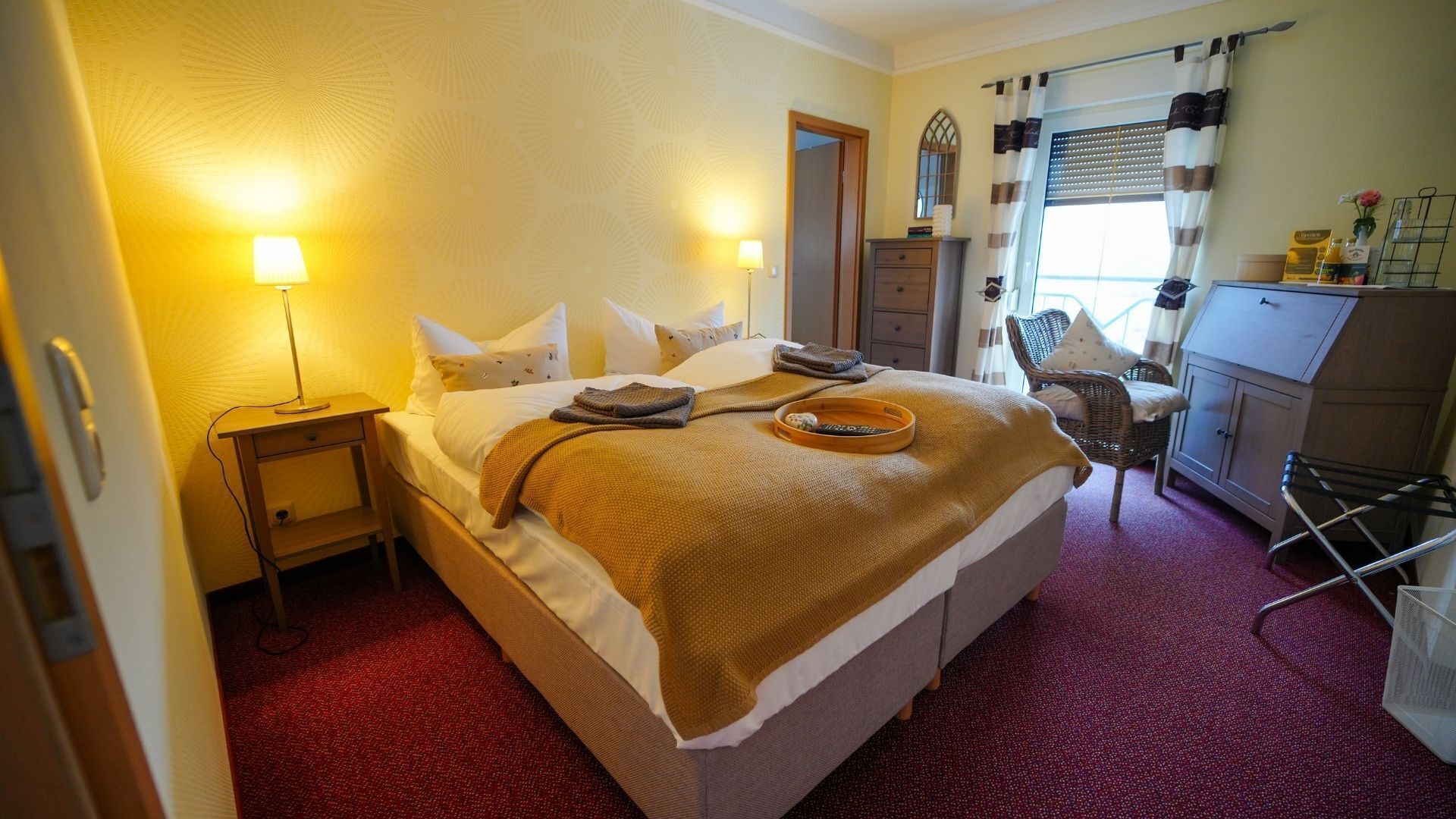 Una habitación de hotel con cama, lámparas de noche, una silla, un escritorio y una ventana con cortinas.