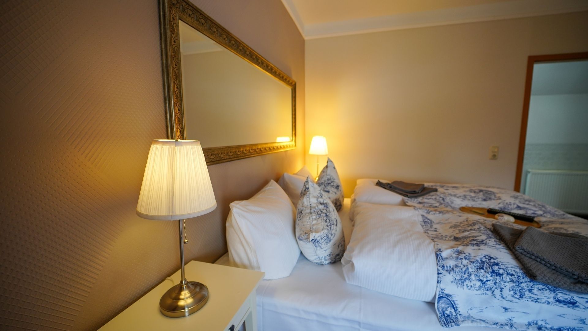 Habitació d'hotel amb un llit, una làmpada de nit, un mirall i una tauleta de nit.