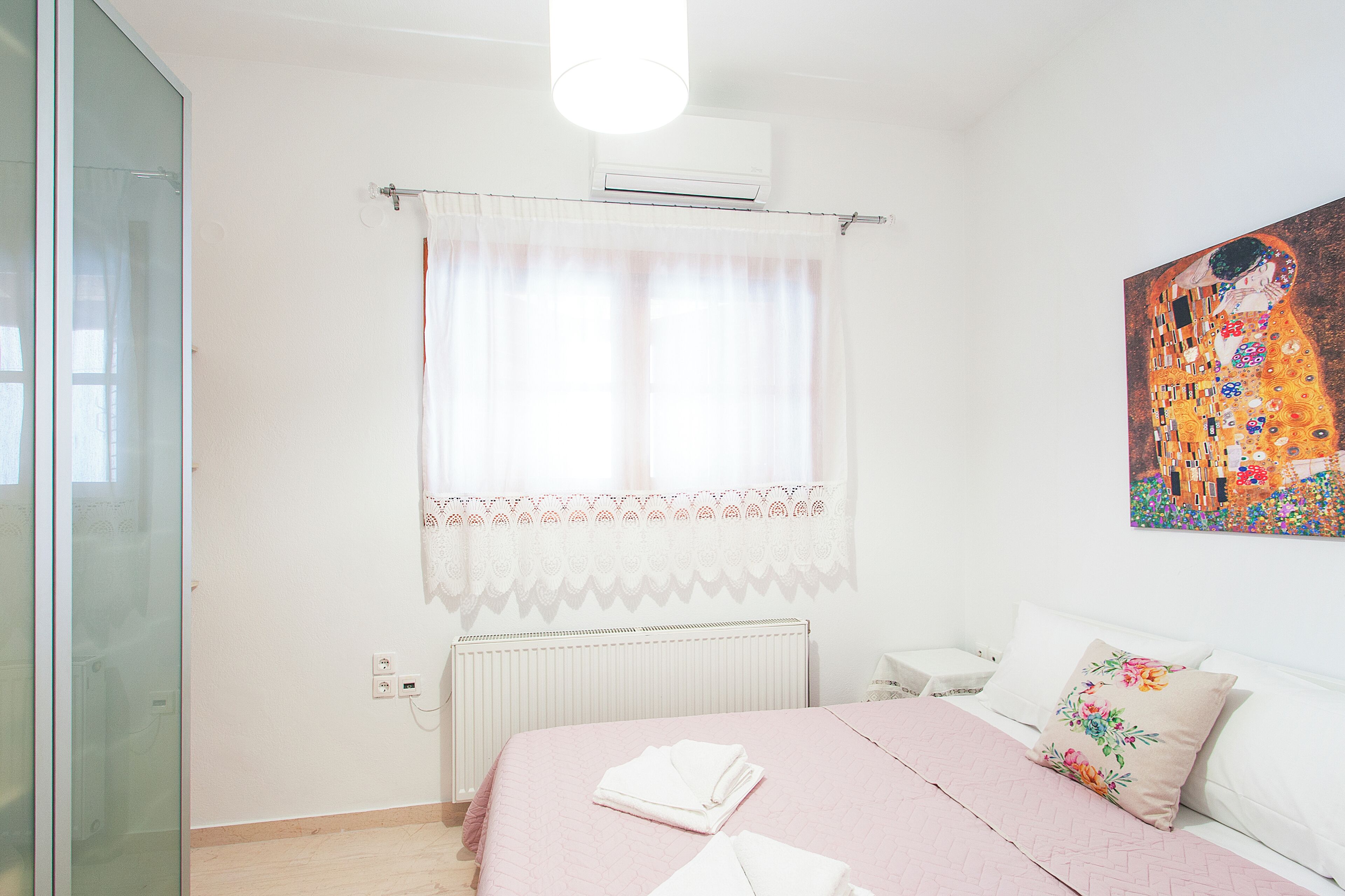 A bedroom with a bed, a radiator, a window with curtains, and a painting on the wall.