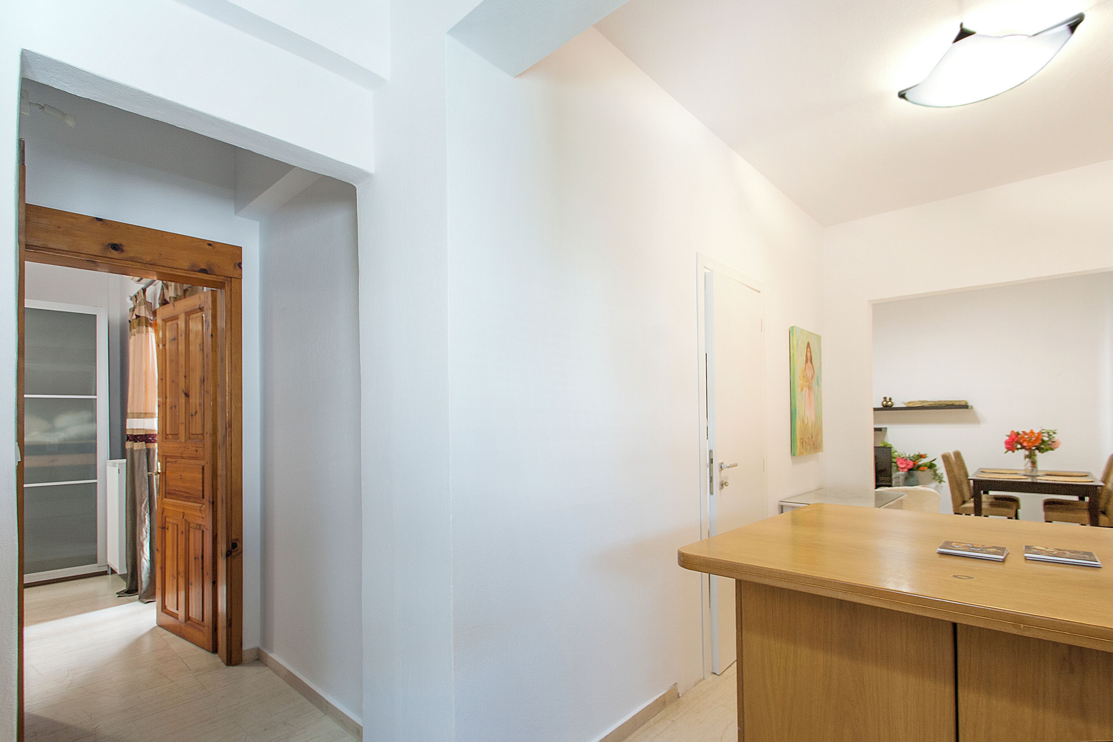 Un pasillo con una puerta de madera, una puerta blanca y un comedor con mesa y sillas.