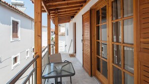 Un balcón con una mesa y sillas de vidrio, contraventanas de madera y suelo de baldosas.