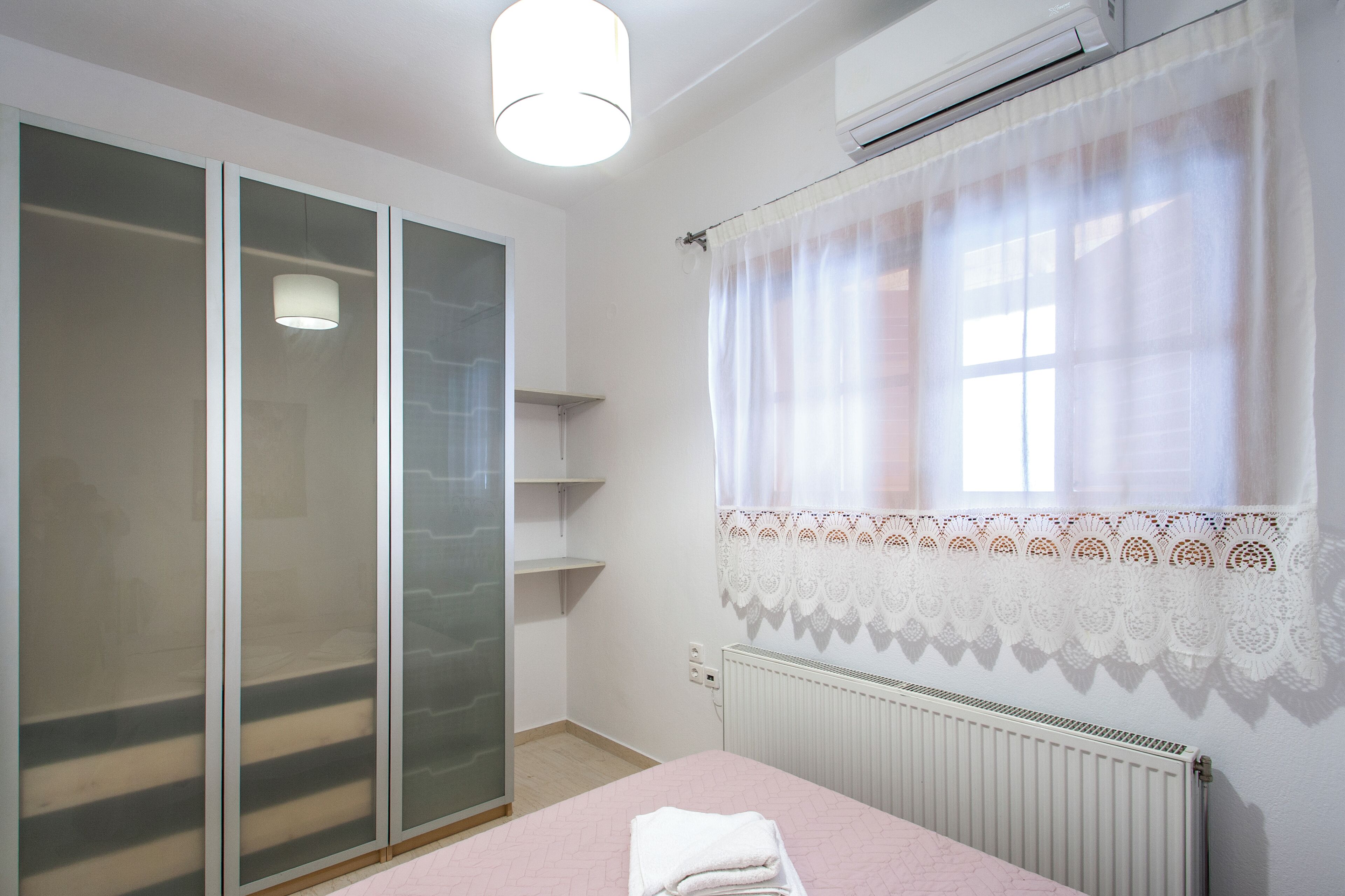 A bedroom with a bed, a wardrobe, a radiator, and a window with curtains.