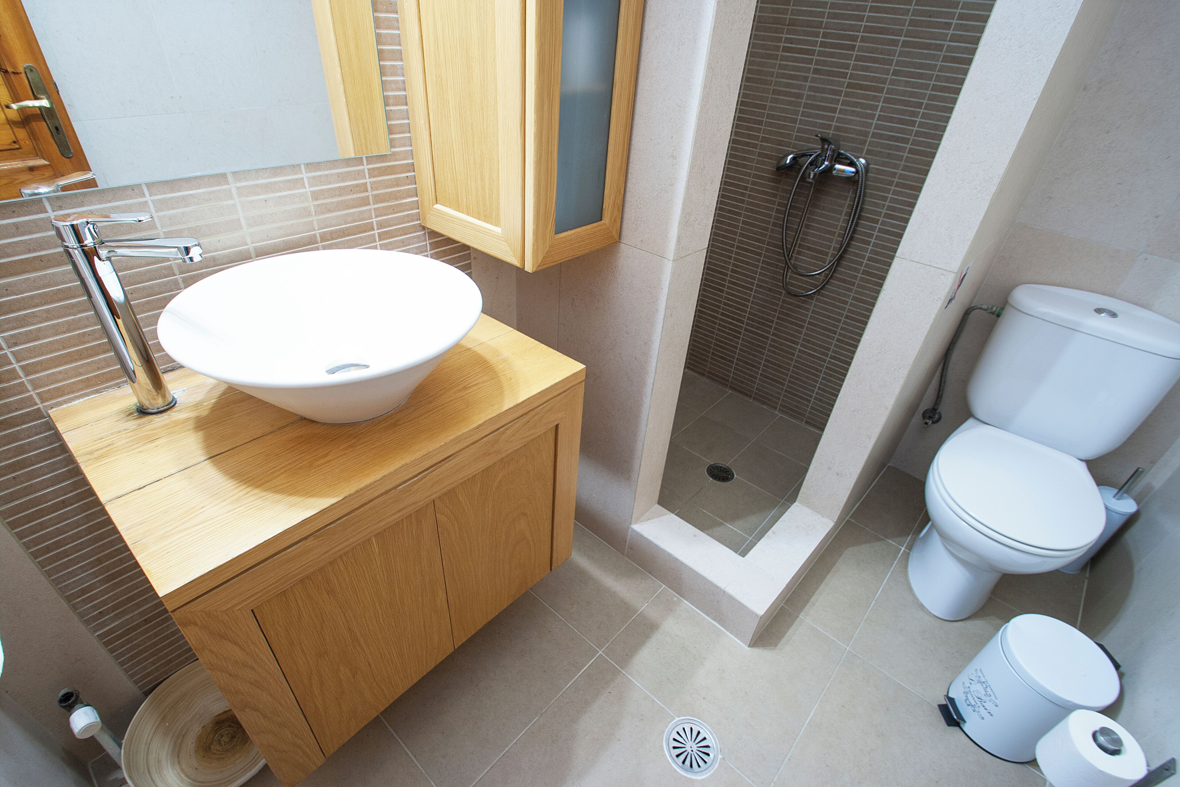 A bathroom with a wooden vanity, a white sink, a shower enclosure, and a toilet.