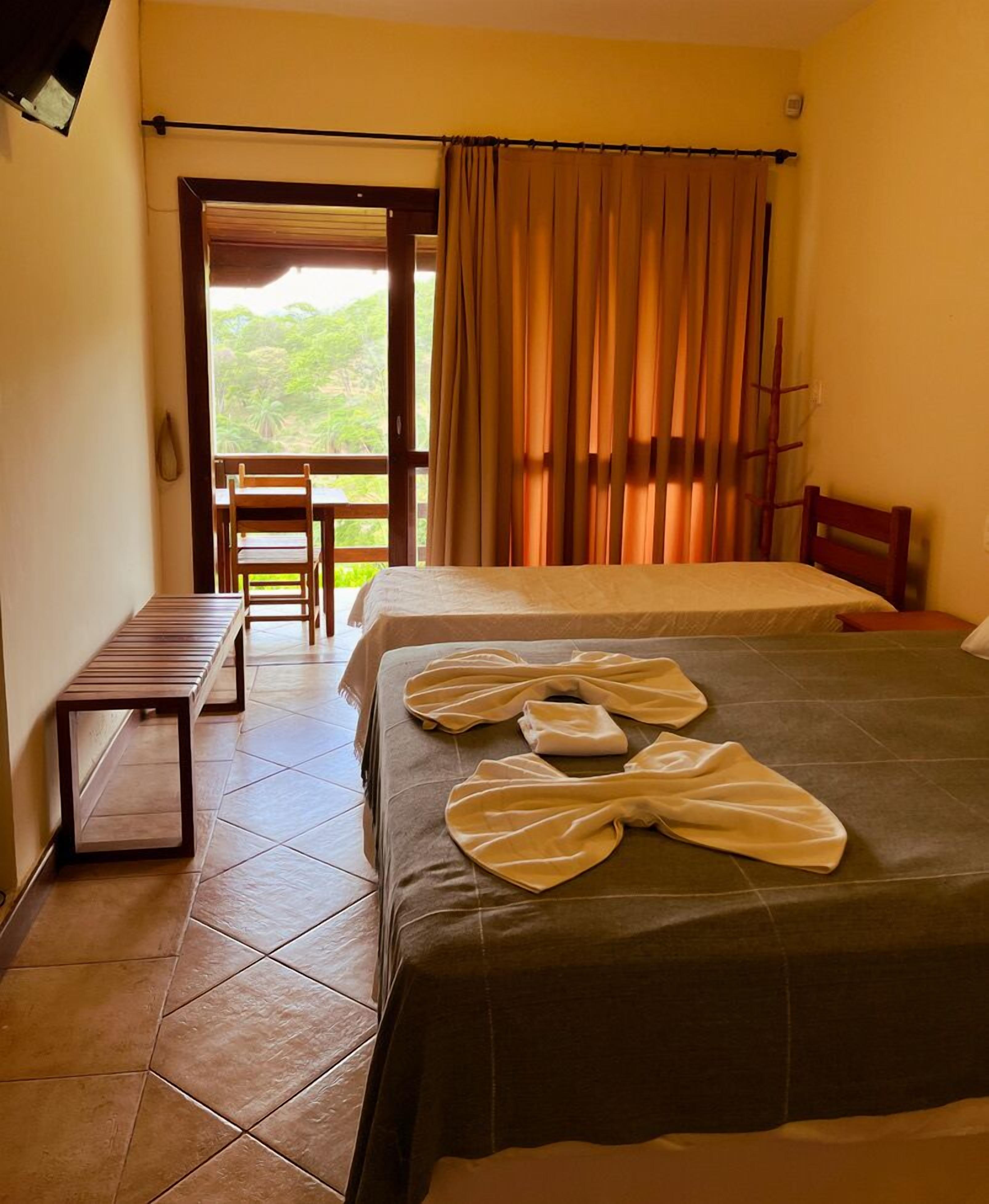 A hotel room with a bed, a bench, and a view of greenery outside.
