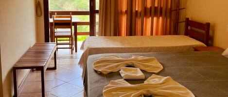 A hotel room with a bed, a bench, and a view of greenery outside.