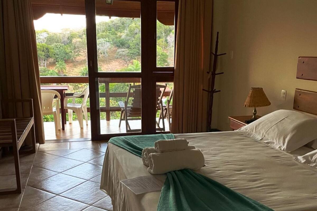 A hotel room with a bed, a green throw blanket, and a view of the outdoors through a glass door.