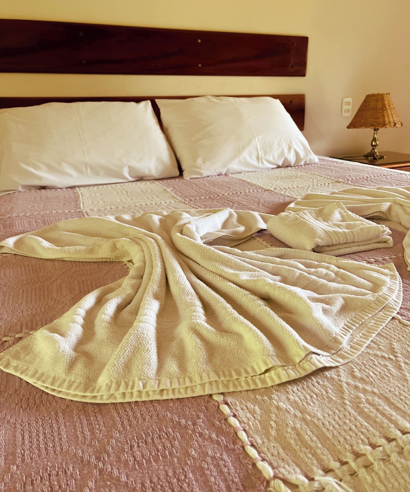 A bed with a pink quilt, white pillows, and a bedside lamp.