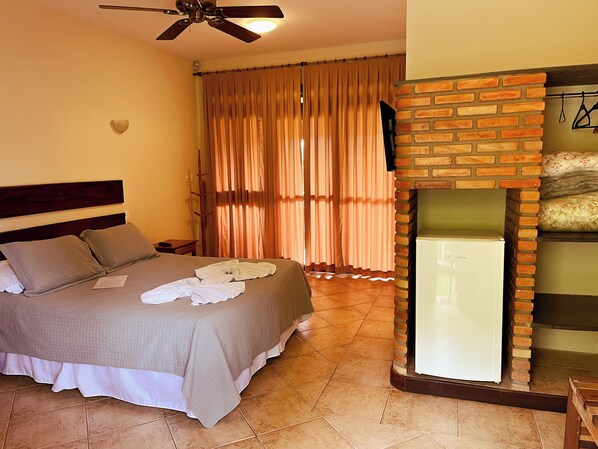 Una habitación de hotel con cama, ventilador de techo, chimenea de ladrillo y cortinas.