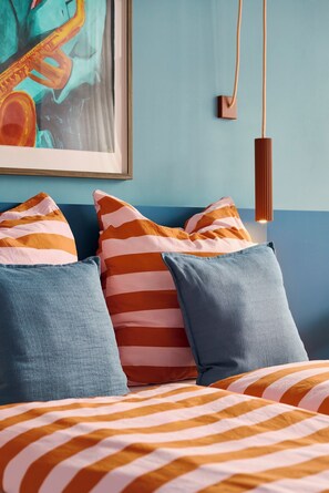 A bed with striped bedding, pillows, and a framed artwork above.