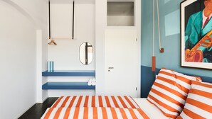 A bedroom with a bed, striped pillows, a mirror, a shelf with books, and a painting. - Poets Place | Design Apartment in Kreuzberg (Berlin)