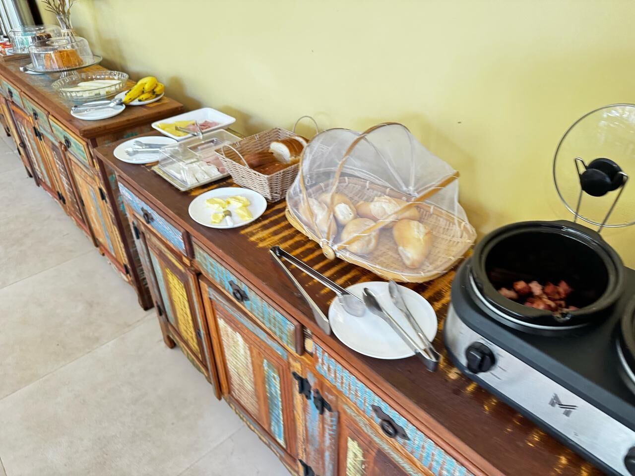 A buffet setup with various food items and utensils on a wooden table against a yellow wall.