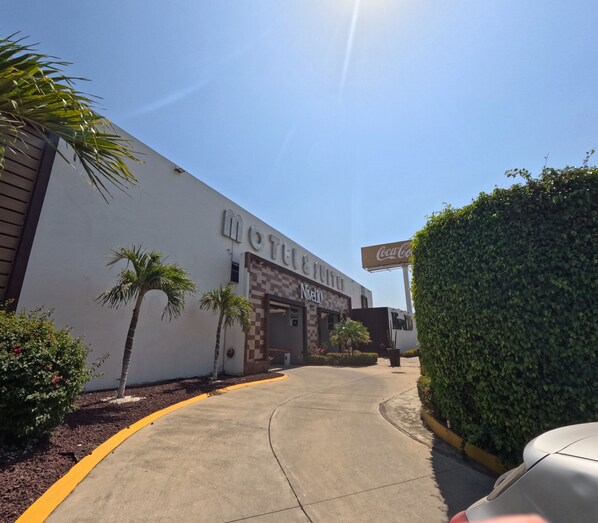A motel with a Coca-Cola sign, palm trees, and a clear sky.