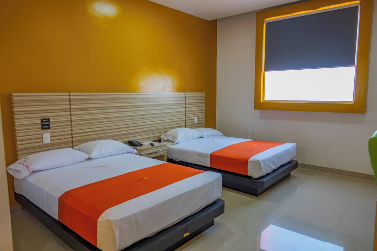 A hotel room with two beds, a window, and a nightstand with a phone.