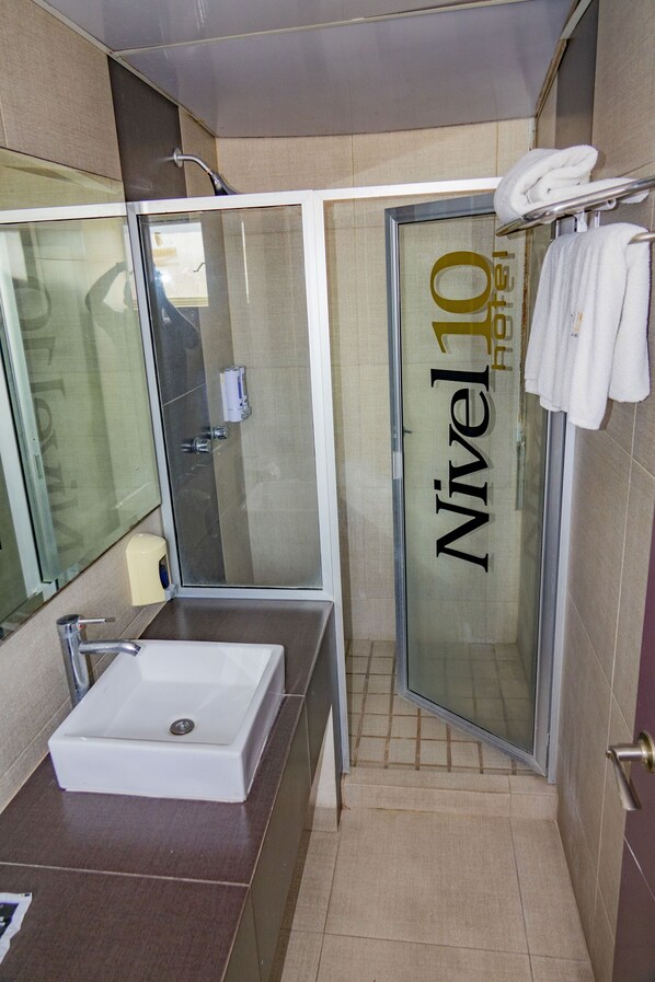 A bathroom with a glass shower door, a sink, and a towel rack. - Motel & Hotel Nivel 10 (Manzanillo)
