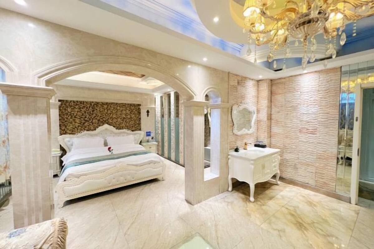 A bedroom with a large bed, a vanity, and a chandelier.