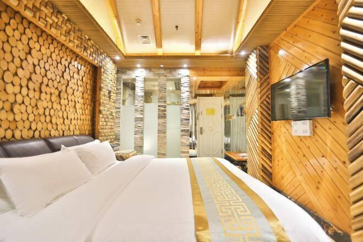 A hotel room with a bed, wooden wall paneling, a television, and a stone wall.