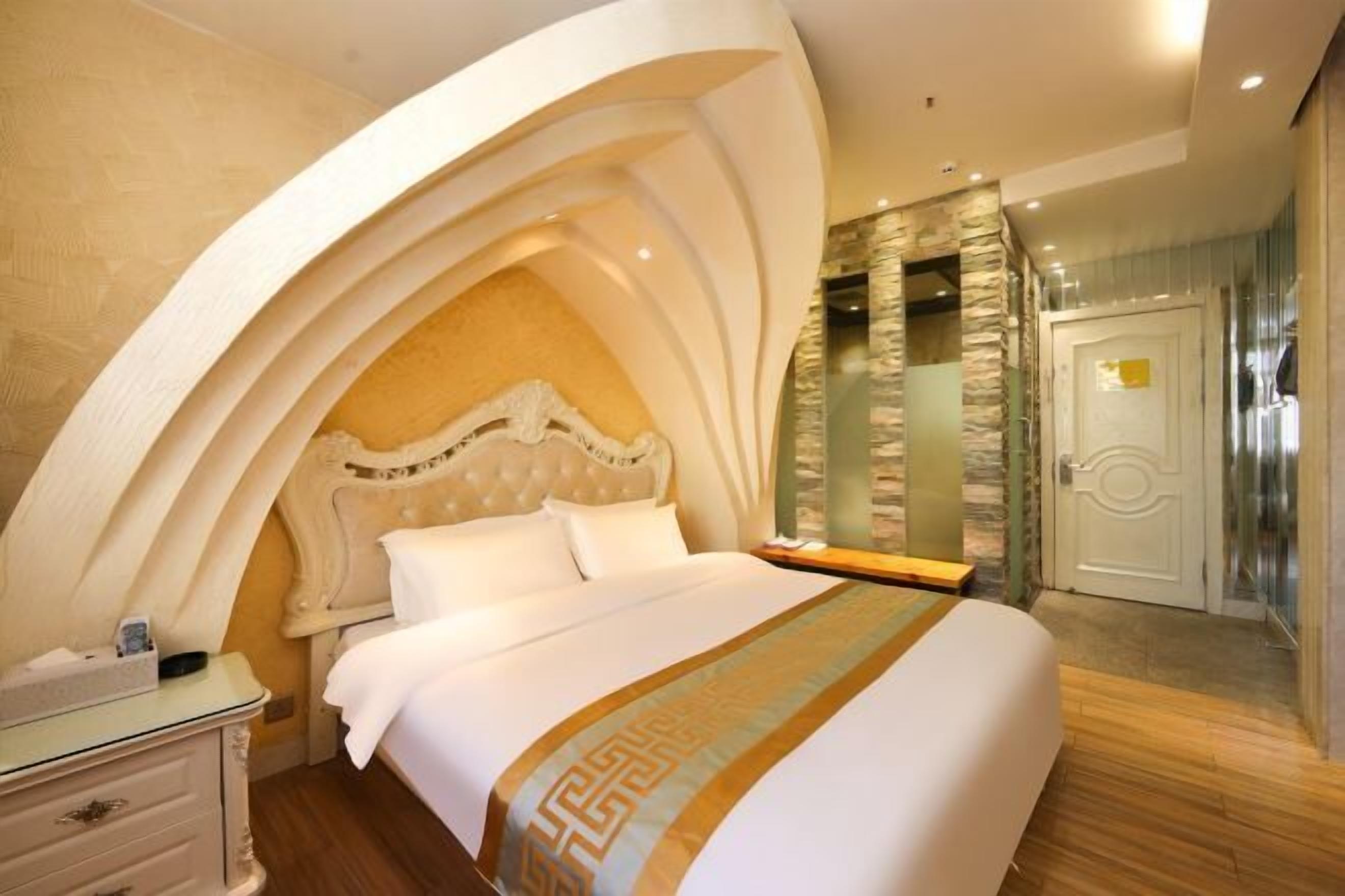 A bedroom with a large bed, an arched ceiling, a stone wall, and a door.