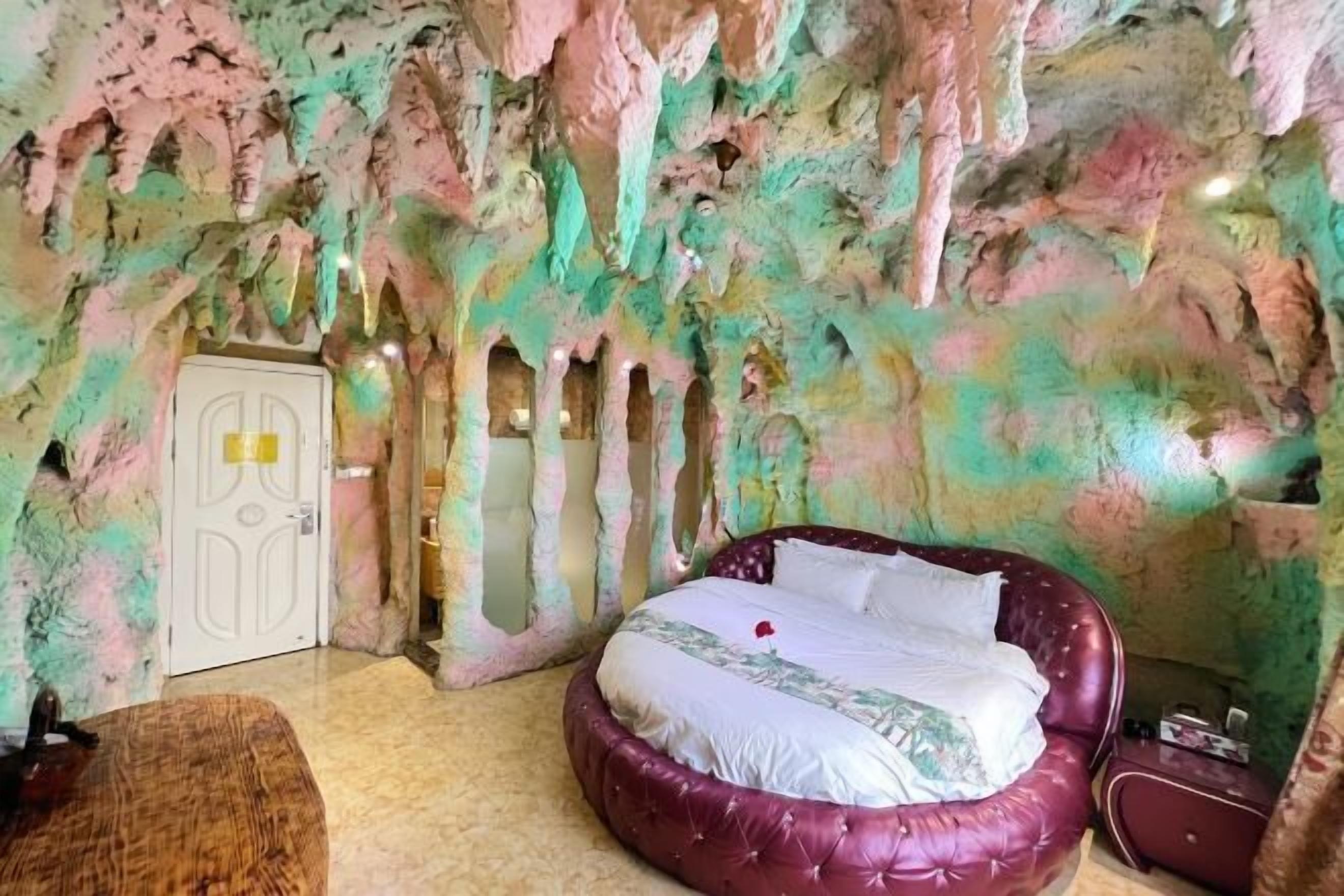 A room with a bed, a door, and a wall with a cave-like texture.