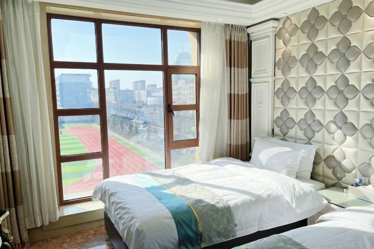 A hotel room with a large window, a bed, a nightstand, and a decorative headboard.