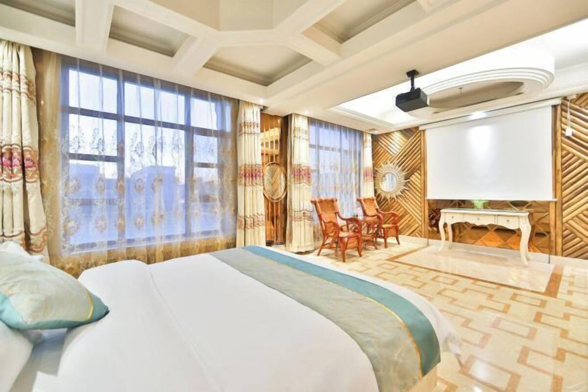 A hotel room with a large bed, a TV, a dining table with chairs, and a decorative wall.
