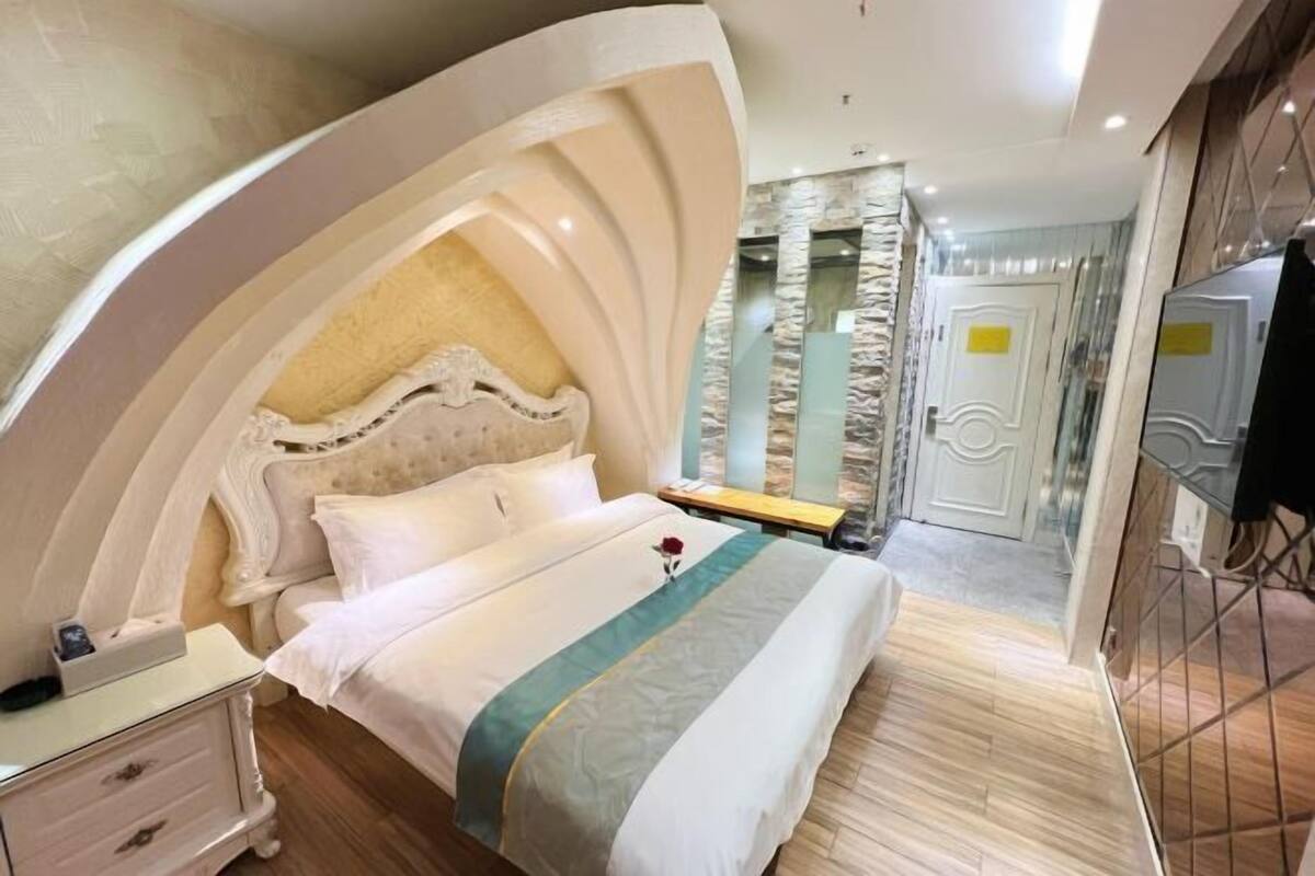 A bedroom with a large bed, a nightstand, a dresser, and a mirror.