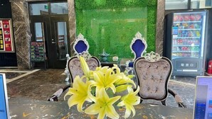 A lobby with a green wall, marble flooring, a vending machine, and two ornate chairs with a vase of yellow lilies. - No.5 Theme Hotel (Yanji)
