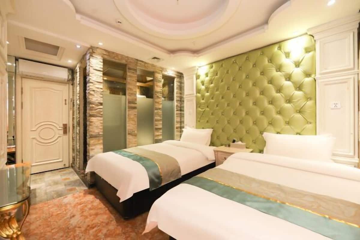 A hotel room with two beds, a stone wall, a green upholstered headboard, and a glass table.
