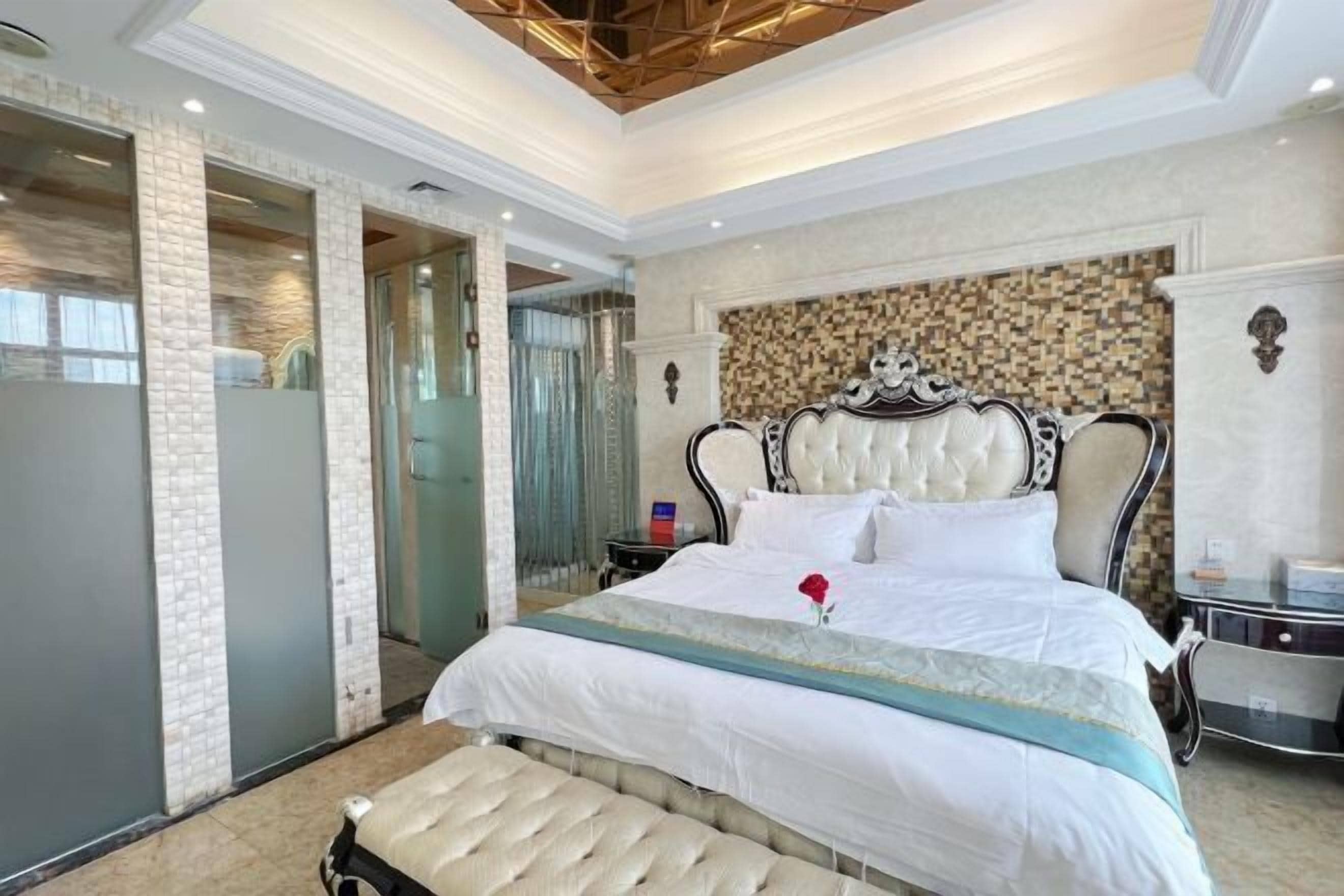 A hotel room with a large bed, a bench, a nightstand, and a mirror.