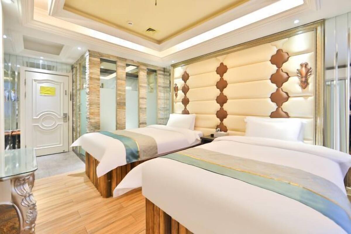 A hotel room with two beds, a wooden headboard, a glass door, and a small table.