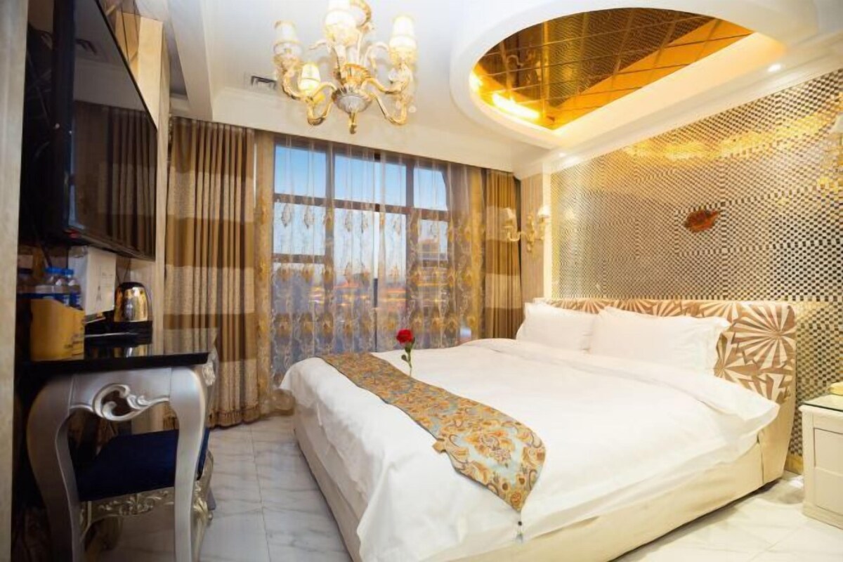 A hotel room with a large bed, a desk, and a chandelier.