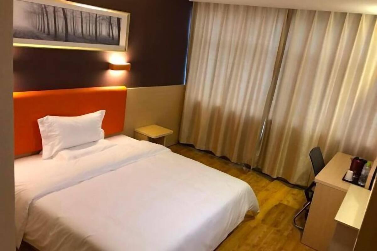 A hotel room with a large bed, a nightstand, a desk, and a window with curtains.